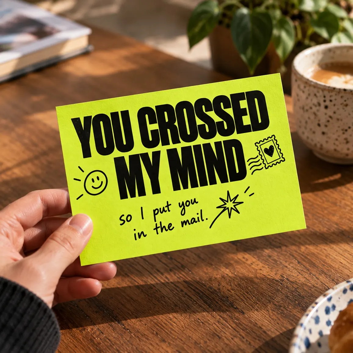 Printed 'You crossed my mind' postcard held in hand at a sunny breakfast table